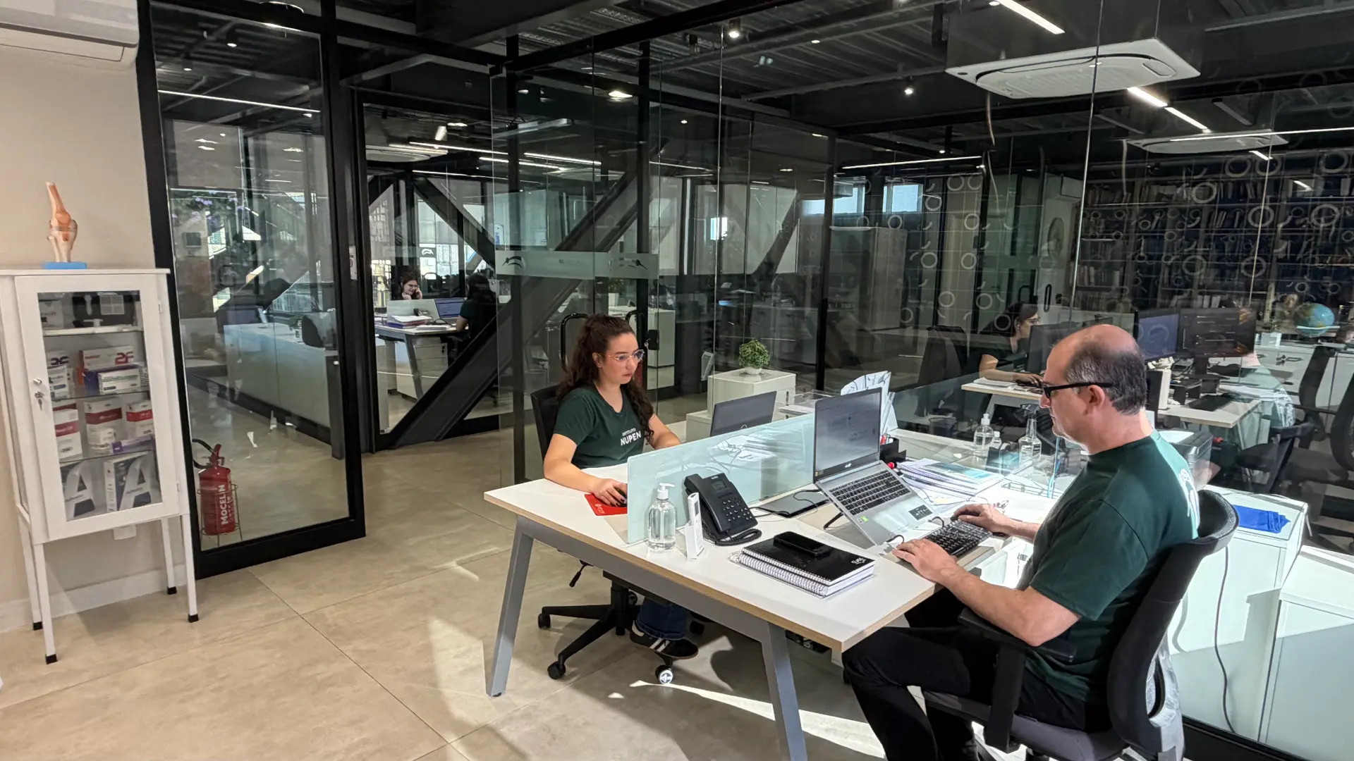 Equipe do Instituto Nupen trabalhando em estações de trabalho no escritório com divisórias de vidro