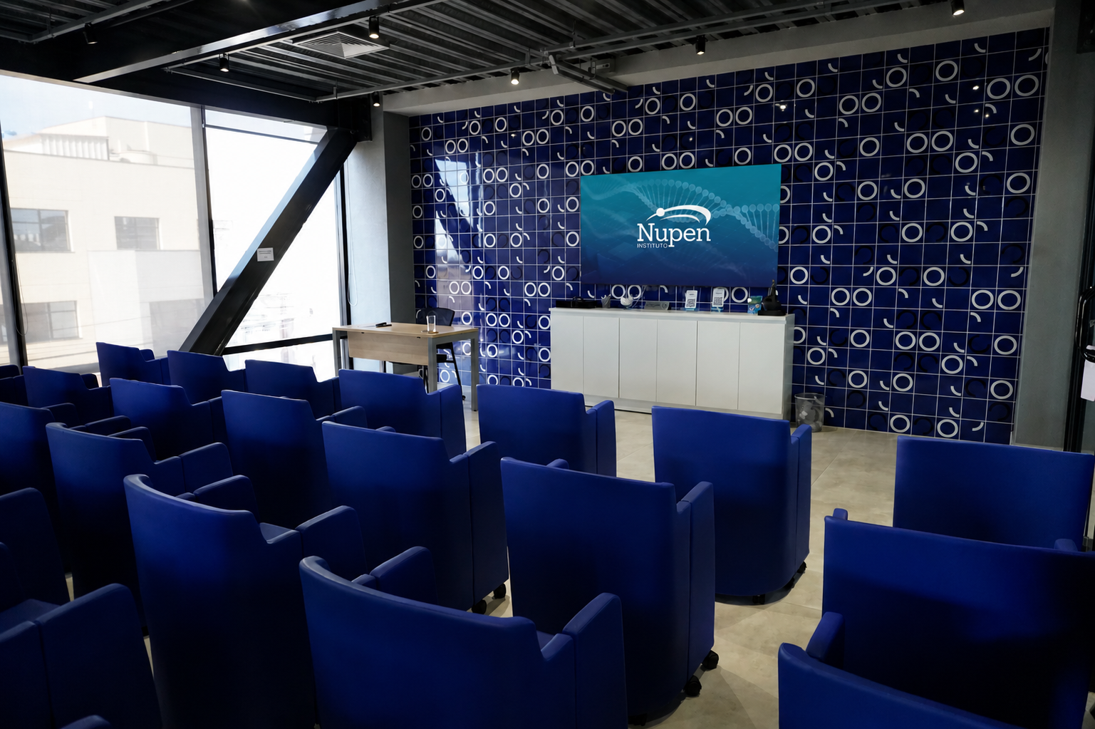 Auditório do Instituto Nupen com poltronas azuis e painel de apresentação